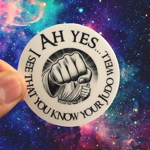 May include: A white circular sticker with the text "AH YES... I SEE THAT YOU KNOW YOUR JUDO WELL" encircling a black and white illustration of a clenched fist. The background is a colorful galaxy.