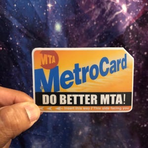May include: A yellow and blue MetroCard with the text "MTA MetroCard" and "DO BETTER MTA!"  The card has instructions to insert it "this way / This side facing you".