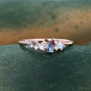 May include: A rose gold band ring with a cluster of blue and white gemstones. The ring features a pear-shaped blue gemstone in the centre, surrounded by smaller round and rectangular gemstones.