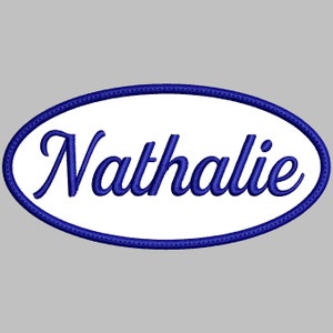 Puede incluir: Un parche ovalado blanco con un contorno azul y el nombre "Nathalie" bordado en letras cursivas azules.
