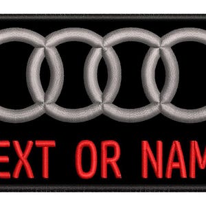 Puede incluir: Parche bordado con el logotipo de Audi, cuatro anillos plateados entrelazados, sobre un fondo negro. Las palabras "TEXTO O NOMBRE" están bordadas en rojo debajo del logotipo. El parche tiene un borde negro.