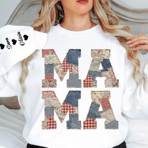 Può includere: Felpa bianca con la scritta "MAMA" in lettere patchwork. Le lettere sono realizzate in denim, tessuti floreali e a quadri. La manica sinistra riporta i nomi "Hazel", "Sara" e "Olivia" con simboli a cuore.