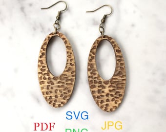 May include: A pair of wooden earrings with a leopard print design. The earrings are oval shaped with a cutout in the center. The earrings are hanging from gold-colored hooks. The text "Digital download Earrings file for laser cutting" is at the top of the image. The text "SVG PDF PNG JPG" is at the bottom of the image.