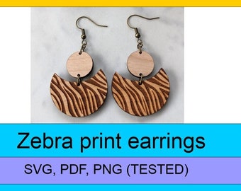May include: A pair of wooden earrings with a zebra print design. The earrings are made of two pieces, a circle and a crescent shape. The earrings are attached to gold-colored hooks.