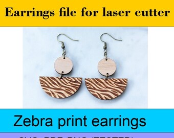 May include: A pair of wooden earrings with a zebra print design. The earrings are made of two pieces: a half-circle with a zebra print and a smaller circle above it. The earrings are attached to gold-colored hooks. The text "DIGITAL DOWNLOAD Earrings file for laser cutter Zebra print earrings SVG, PDF, PNG (TESTED)" is displayed below the earrings.