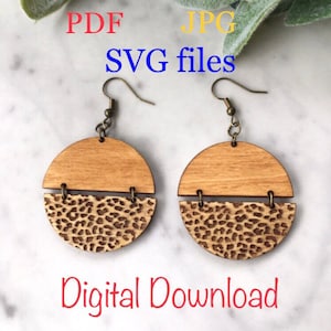 May include: A pair of laser cut wooden earrings with a leopard print design. The earrings are made of two pieces of wood, one with a natural wood finish and the other with a leopard print design. The earrings are attached to gold-colored hooks. The image includes the text "PDF, JPG, SVG files, Digital Download, Laser cut earrings".