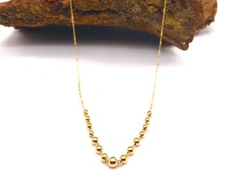 Op de afbeelding: Een gouden ketting met een ketting en ronde kralen. De ketting wordt gepresenteerd op een stuk hout.