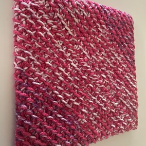 May include: A pink and white knitted square with a diagonal pattern.