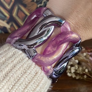 May include: A chunky bracelet with a chain link design. The bracelet features translucent purple links and silver-colored metal links. The bracelet is worn on a wrist, with a cream-colored sweater sleeve visible.