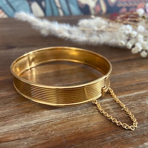 Pulseira vintage dourada com dobradiça e textura canelada, com corrente de segurança.
