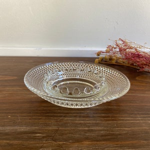 Peut inclure: Un cendrier en verre transparent avec un motif en diamant et un anneau central surélevé. Le cendrier est posé sur une surface en bois.