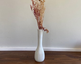 Pode incluir: Um vaso de cerâmica branco com um design canelado, contendo um buquê de flores secas em tons de marrom e rosa.