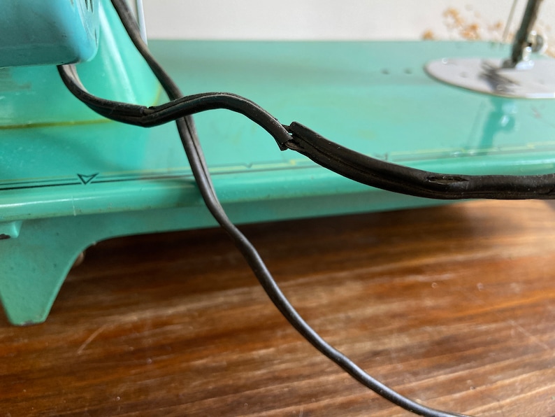 May include: A vintage turquoise sewing machine with a black electrical cord. The cord is frayed and worn.