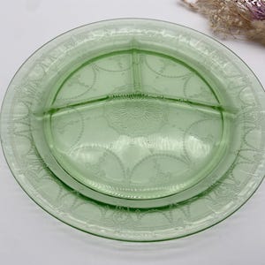 May include: A vintage green glass divided serving plate. The plate has a circular shape with three compartments and a decorative etched design around the rim and in the center. The plate is made of a translucent green glass.