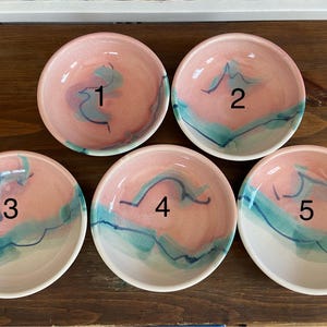 Puede incluir: Cinco cuencos pequeños de cerámica con un esmalte rosa y blanco y detalles azules y verdes. Los cuencos están numerados del 1 al 5.