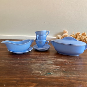 Puede incluir: Un juego de té de plástico azul para niños con una salsera, una cacerola con tapa y tres tazas y platillos.