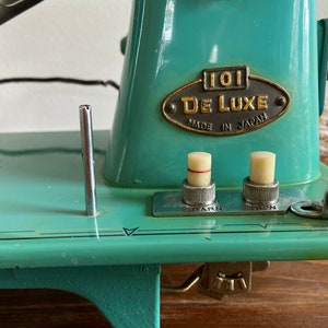 May include: A turquoise blue vintage sewing machine with a metal plate that reads "101 De Luxe Made in Japan". The machine has two knobs, one labeled "Darn" and the other labeled "Sew".