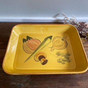 Puede incluir: Bandeja rectangular amarilla con un diseño de verduras pintado a mano. La bandeja presenta ilustraciones de cebollas, una seta y otras verduras. La bandeja es de color amarillo cálido con un borde marrón.