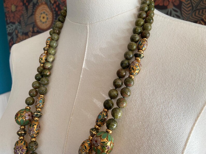 Puede incluir: Un collar de doble cadena hecho de cuentas de piedra verde y marr&oacute;n con detalles dorados y cuentas redondas m&aacute;s grandes, multicolores, con dise&ntilde;os florales.