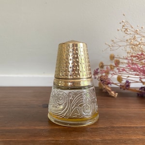 May include: A gold and clear glass bottle with a decorative design. The bottle is shaped like a thimble and has a gold top.