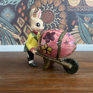 大きな卵の手押し車を押すビンテージ擬人化ウサギ、春に飾られたセラミックイースターエッグ、季節の小物皿、キッチュなウサギ