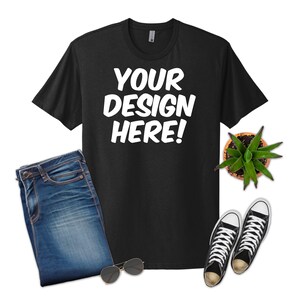 May include: Black t-shirt with the text "YOUR DESIGN HERE!" in white, paired with blue jeans, black and white sneakers, sunglasses, and a small potted succulent. A casual, everyday outfit.