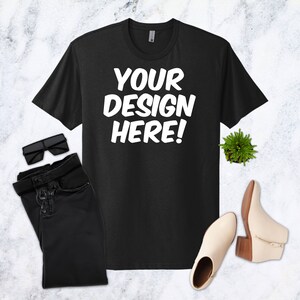 May include: Black t-shirt with the text "YOUR DESIGN HERE!" in white, paired with black sunglasses, black jeans, a small green plant, and cream-colored ankle boots with a wooden heel.