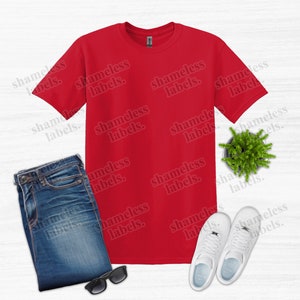 K&ouml;nnte beinhalten: Ein rotes T-Shirt, blaue Jeans, wei&szlig;e Turnschuhe, eine Sonnenbrille und eine kleine Topfpflanze sind auf einer wei&szlig;en Oberfl&auml;che angeordnet. Der Text "shameless labels" wiederholt sich im Bild. Dieses Bild deutet auf ein l&auml;ssiges Outfit hin.