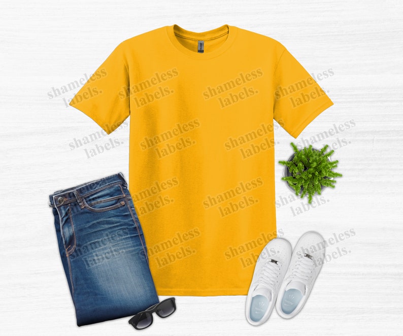 K&ouml;nnte beinhalten: Draufsicht mit einem senfgelben T-Shirt, gefalteten blauen Jeans, einer schwarzen Sonnenbrille, einer kleinen Topfpflanze und wei&szlig;en Turnschuhen. Der Text "shameless labels" ist als Wasserzeichen im Bild.