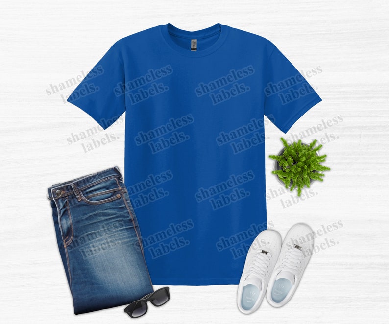 K&ouml;nnte beinhalten: Ein k&ouml;nigsblaues T-Shirt, gefaltete Jeans, eine schwarze Sonnenbrille, wei&szlig;e Turnschuhe und eine kleine Topfpflanze sind auf einer wei&szlig;en Oberfl&auml;che angeordnet. Auf dem T-Shirt steht der Text "shameless labels".