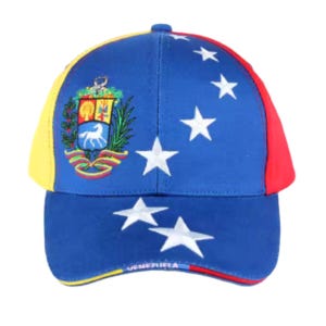 Puede incluir: Una gorra de béisbol azul con una visera amarilla, roja y azul. La gorra presenta un patrón de estrellas blancas y el escudo de armas venezolano bordado en la parte delantera. El texto "VENEZUELA" está bordado en la visera.