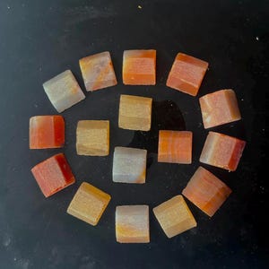 Puede incluir: Una colección de 15 pequeñas baldosas cuadradas decorativas con una variedad de patrones y colores, incluyendo naranja, rojo, blanco y dorado.