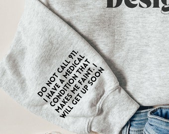 May include: A grey sweatshirt with the text "Rileigh Creates Design" printed on the front. The left sleeve has the text "DO NOT CALL 911. I HAVE A MEDICAL CONDITION THAT MAKES ME FAINT. I WILL GET UP SOON" printed on it.