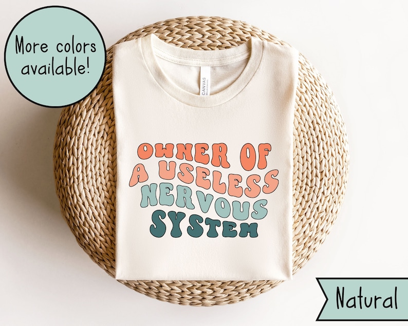 May include: A white t-shirt with the text "OWNER OF A USELESS NERVOUS SYSTEM" in a retro, colorful font. The text is in shades of blue, green, orange, and pink.