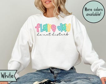 May include: White sweatshirt with the text "Flare Day do not disturb" in colorful bubble letters. The sweatshirt has long sleeves and a crew neck. A green circle with the text "More colors available!" is in the upper right corner.