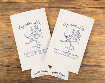 May include: Two white can coolers with blue text and graphics. The text reads "Apres Ski Est. '25 Emily's Bachelorette Last Toast on the Slopes". The graphic is a woman skiing down a mountain with a cocktail in her hand.