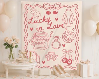 May include: A cream-colored tapestry with a pink outline of various wedding-themed illustrations, including dice, cherries, a bridal veil, a slot machine, a ring, a poker chip, and the text "Lucky in Love." The scene is decorated with balloons and flowers.