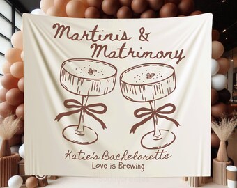 Könnte beinhalten: Ein beigefarbener Stoffhintergrund mit braunem Text, der "Martini's & Matrimony" lautet, und einer Grafik von zwei Martini-Gläsern. Der Text unter den Gläsern lautet "Katie's Bachelorette Love is Brewing".