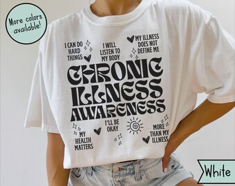 May include: White t-shirt with the words "CHRONIC ILLNESS AWARENESS" in large, black, stylized letters. The shirt also features several phrases and symbols, including "I CAN DO HARD THINGS" and "MY ILLNESS DOES NOT DEFINE ME."