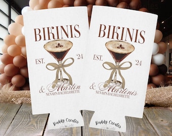 May include: Two white can coolers with brown text that reads "Bikinis & Martinis" and "EST. '24" with a brown illustration of a martini glass with a bow. The bottom of the coolers have the text "Buddy Creates" in black with a floral design.
