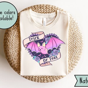 May include: A white t-shirt with a pink and purple bat graphic and the text "Trick or Treat" in a banner. The bat has a cute face and is surrounded by flowers and stars.