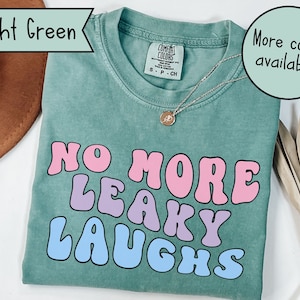 May include: A light green t-shirt with the text "NO MORE LEAKY LAUGHS" in pink, purple, and blue bubble letters.