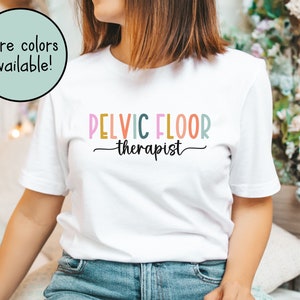 May include: White t-shirt with the text "PELVIC FLOOR therapist" in colorful letters.