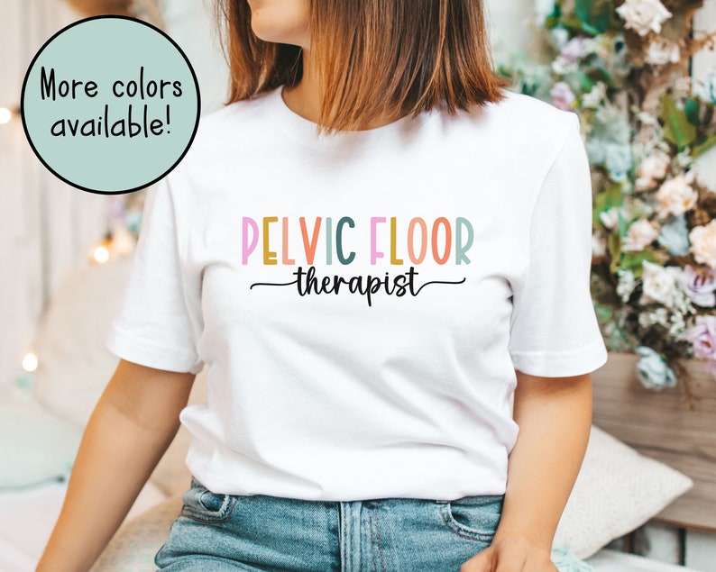 May include: White t-shirt with the text "PELVIC FLOOR therapist" in colorful letters.