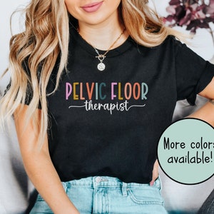 May include: Black t-shirt with the text "Pelvic Floor Therapist" in colorful letters. The text is written in a playful, casual font.  More colors are available.