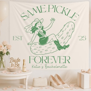 Op de afbeelding: Een crèmekleurige banner met de tekst "SAME PICKLE FOREVER" en een cartoonillustratie van een vrouw met een cowboyhoed die op een augurk rijdt. De banner bevat ook de tekst "EST '25" en "Katie's Bachelorette".