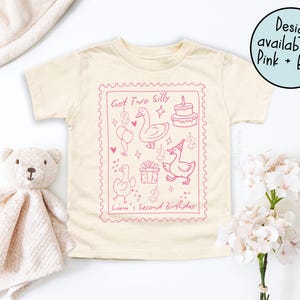May include: A cream-colored toddler t-shirt with a pink graphic design. The design includes the text "Got Two Silly" and "Liam's Second Birthday", along with illustrations of ducks, balloons, a cake, and gifts. The design is available in pink and blue.