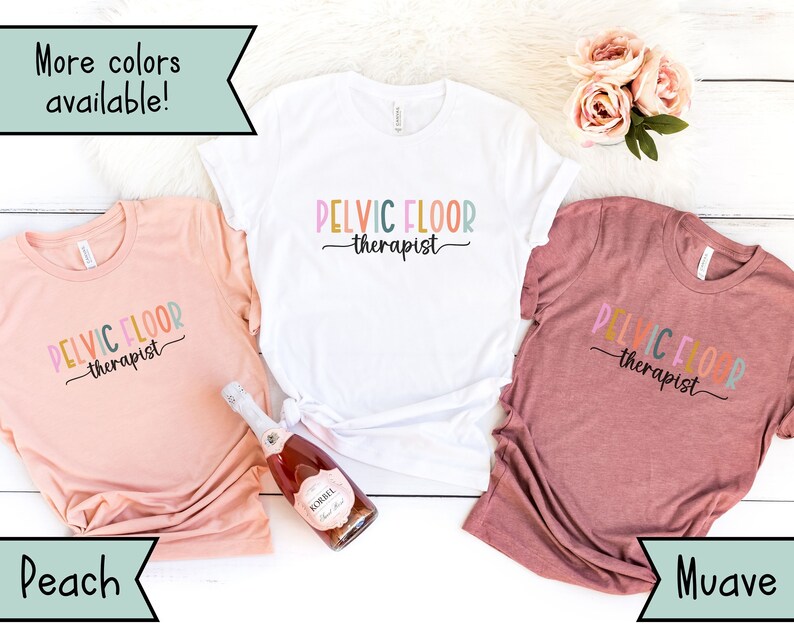 May include: Three t-shirts in peach, white, and mauve colors with the text "PELVIC FLOOR therapist" printed on them. The shirts are displayed on a white wooden surface.