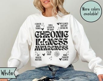 May include: White sweatshirt with the text "CHRONIC ILLNESS AWARENESS" in black. The sweatshirt also features supporting phrases like "I can do hard things" and "My illness does not define me". A green circle indicates "More colors available!"