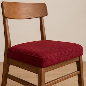 May include: A wooden chair featuring a curved backrest and a square seat upholstered in a textured, deep red fabric. The frame is constructed from medium-toned wood with a visible grain, supported by four straight legs and horizontal support bars.